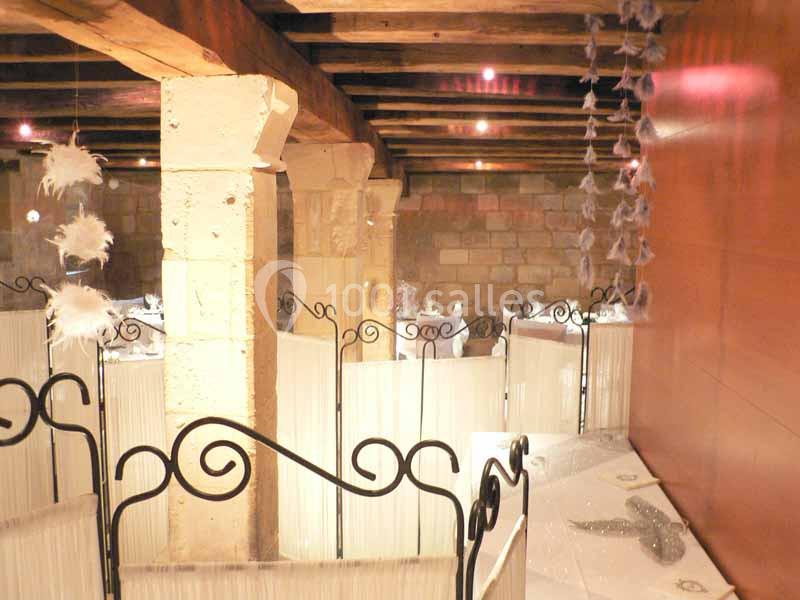 Salle en pierre avec poutres apparentes, séparée par des cloisons décoratives et ornée de plumes suspendues.