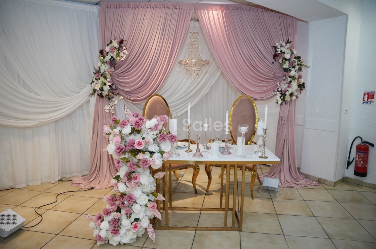 Décoration de table de mariage avec chaises dorées, fleurs roses et blanches, et rideaux drapés roses et blancs.
