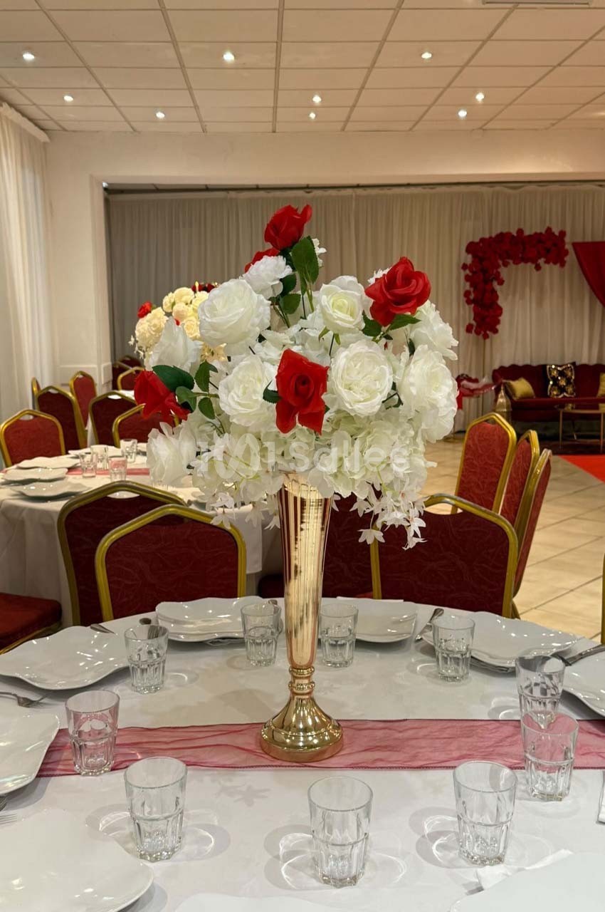 Centre de table avec un vase doré contenant des fleurs blanches et rouges, entouré de vaisselle sur une table dressée.