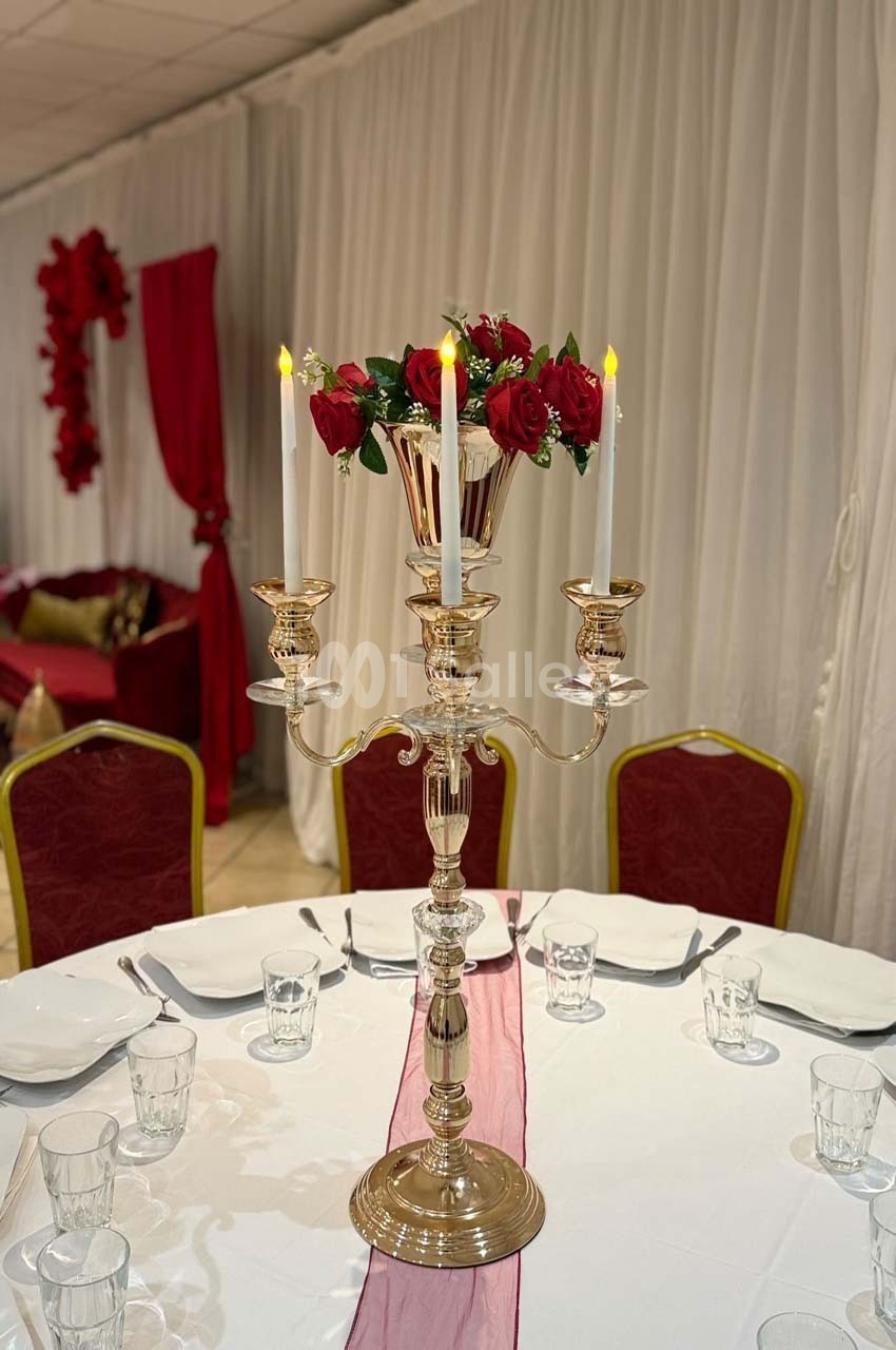 Centre de table avec chandelier doré, bougies allumées et bouquet de roses rouges, sur une table dressée.