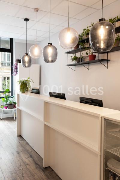 Comptoir d'accueil moderne avec suspensions lumineuses, plantes en décoration et sol en bois clair.