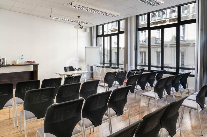 Salle de réunion lumineuse avec des chaises alignées, un tableau blanc et une table devant de grandes fenêtres.