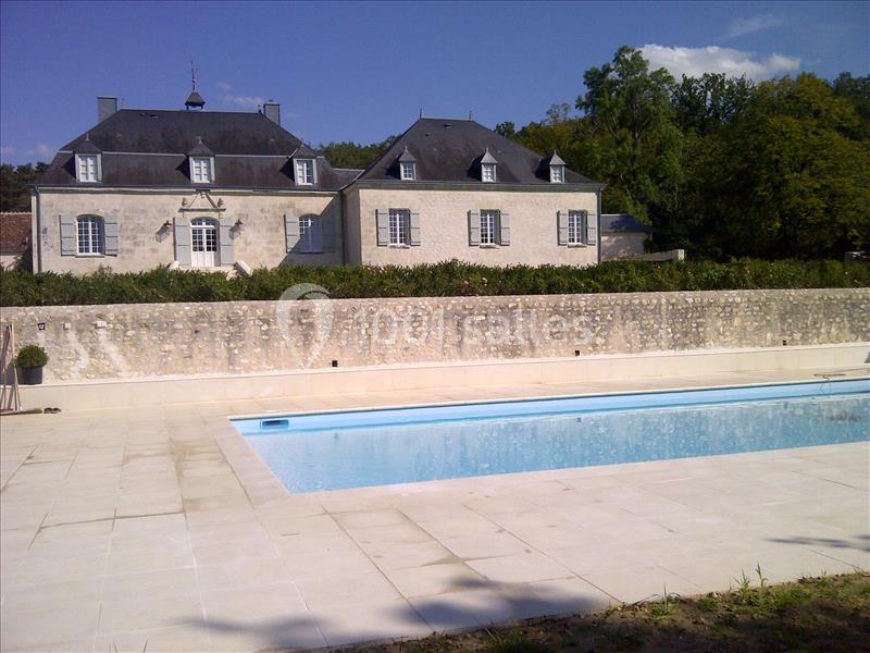 Grande maison en pierre avec toit en ardoise, jardin arboré et piscine entourée d'une terrasse en pierre.