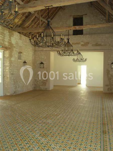 Salle intérieure avec murs en pierre apparente, sol en carreaux décoratifs et plafonds avec poutres et lustres suspendus.