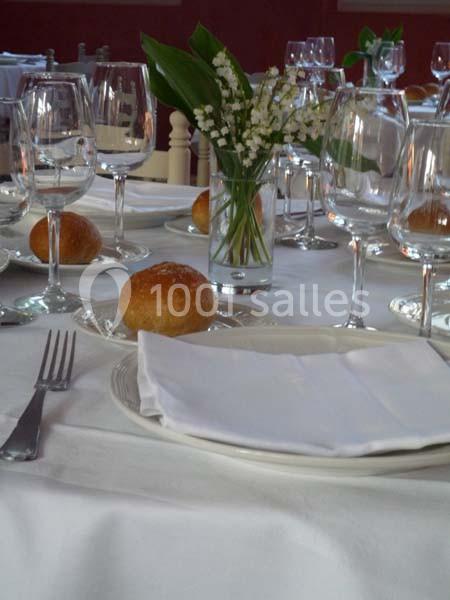 Table dressée avec nappe blanche, couverts, verres, assiettes, petits pains et vase de muguet au centre.