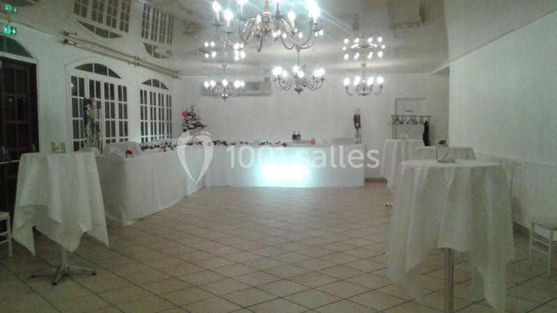 Salle de réception lumineuse avec tables hautes drapées de blanc, lustres et un buffet en arrière-plan.