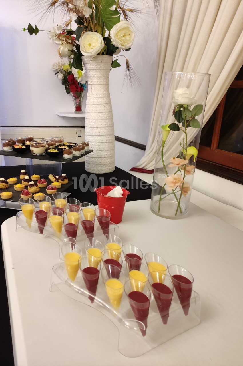 Desserts variés présentés sur une table, avec verrines colorées au premier plan et décor floral en arrière-plan.