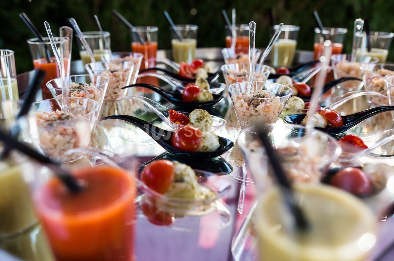 Verrines et cuillères apéritives garnies de légumes, crevettes et sauces, disposées sur une table réfléchissante.
