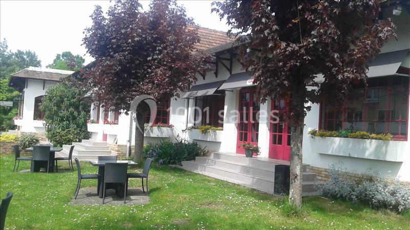 Façade d'un bâtiment avec des fenêtres rouges, entouré d'arbres, de pelouse et de tables en plein air.