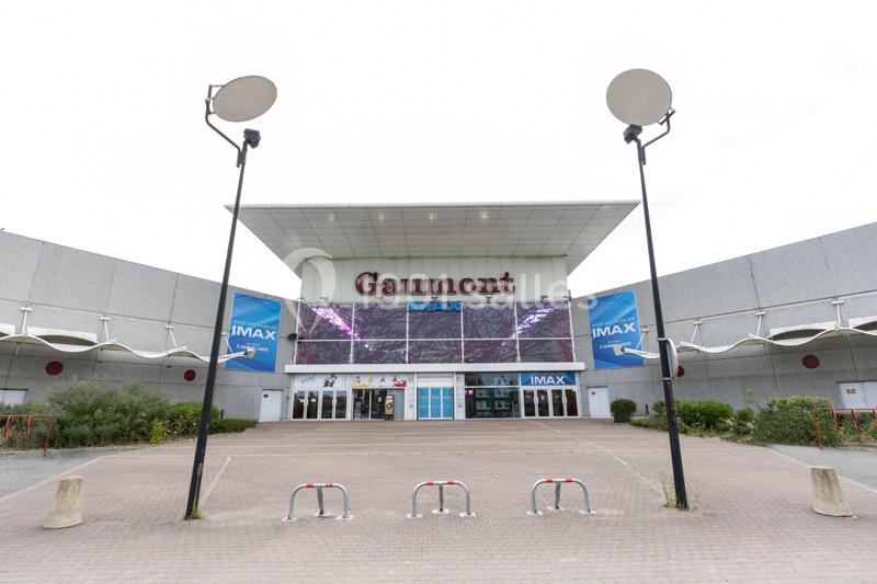 Façade d'un cinéma Gaumont avec des affiches IMAX, un parvis vide et deux lampadaires au premier plan.