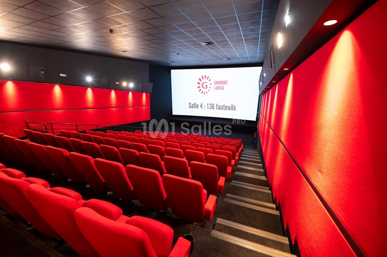 Salle de cinéma moderne avec rangées de sièges rouges, écran blanc affichant ’Salle 4 : 136 fauteuils’.