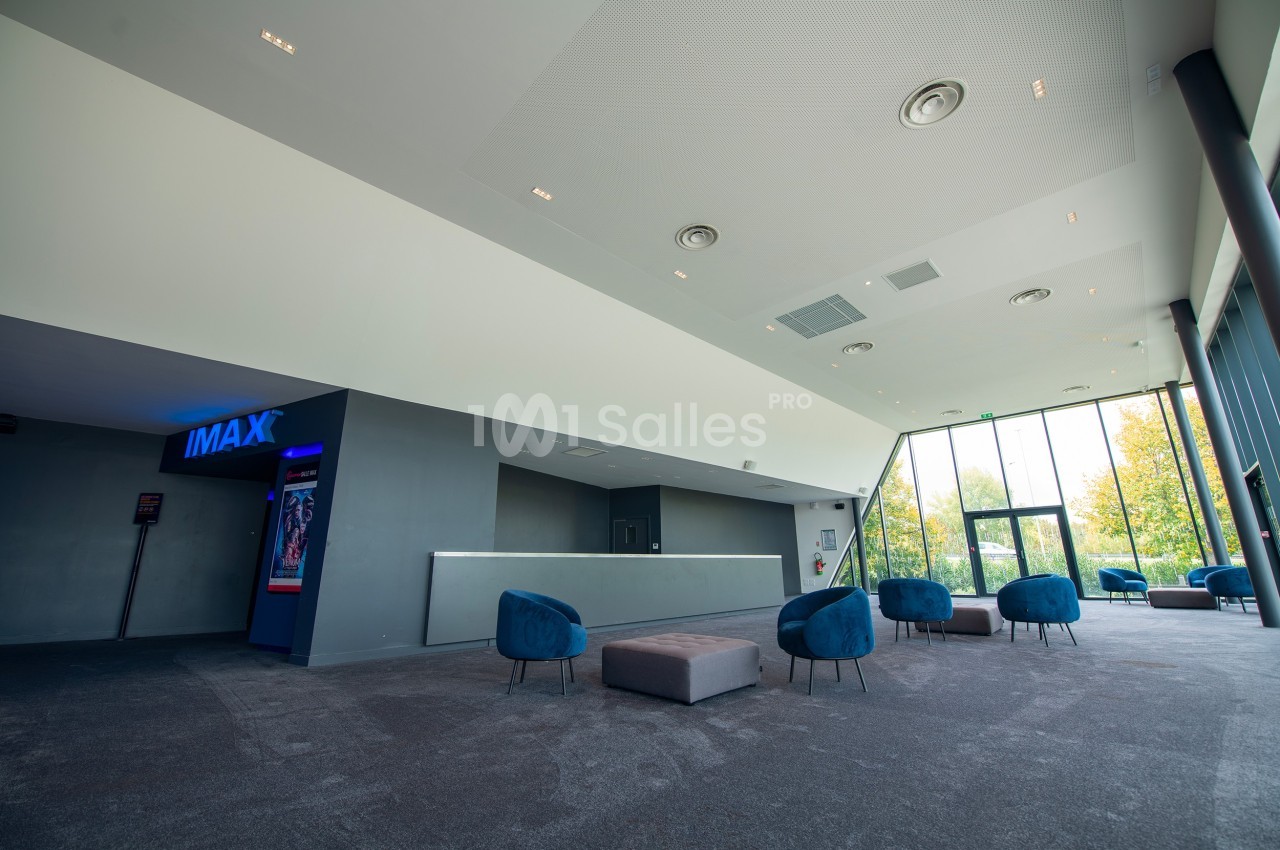 Hall d'entrée spacieux avec fauteuils bleus, lumière naturelle et accès à une salle IMAX visible à gauche.