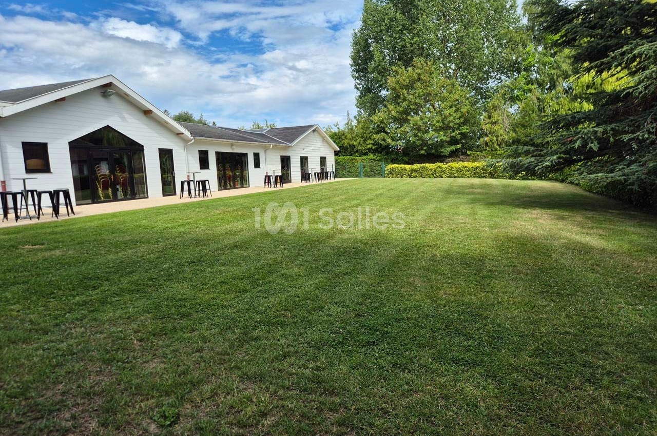 Pelouse bien entretenue devant un bâtiment blanc avec de grandes baies vitrées, entouré d'arbres et de haies.