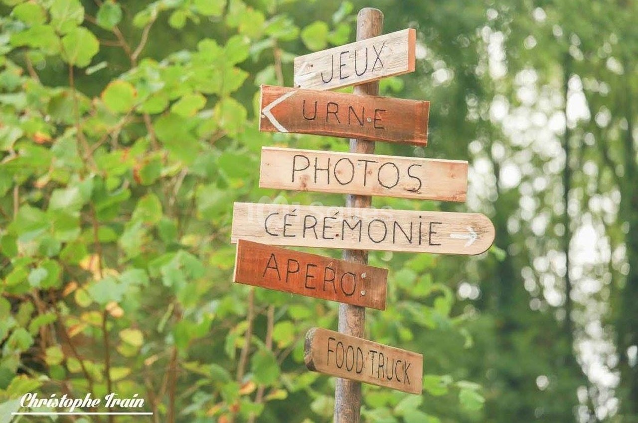 Panneau en bois avec des flèches indiquant des directions pour jeux, urne, photos, cérémonie, apéro et food truck.