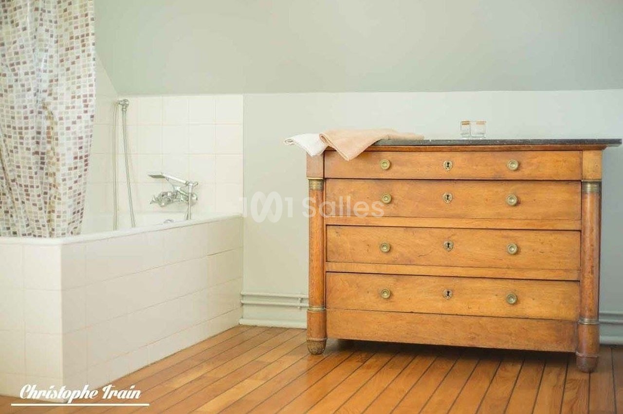 Baignoire avec rideau à motifs et commode en bois sur un sol en parquet dans une salle de bain lumineuse.