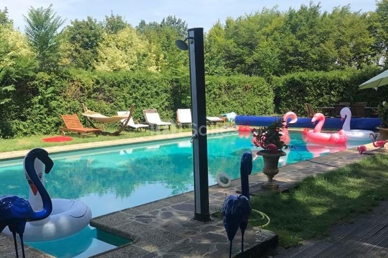 Piscine extérieure entourée de verdure, avec transats, hamacs et bouées en forme de flamants roses.