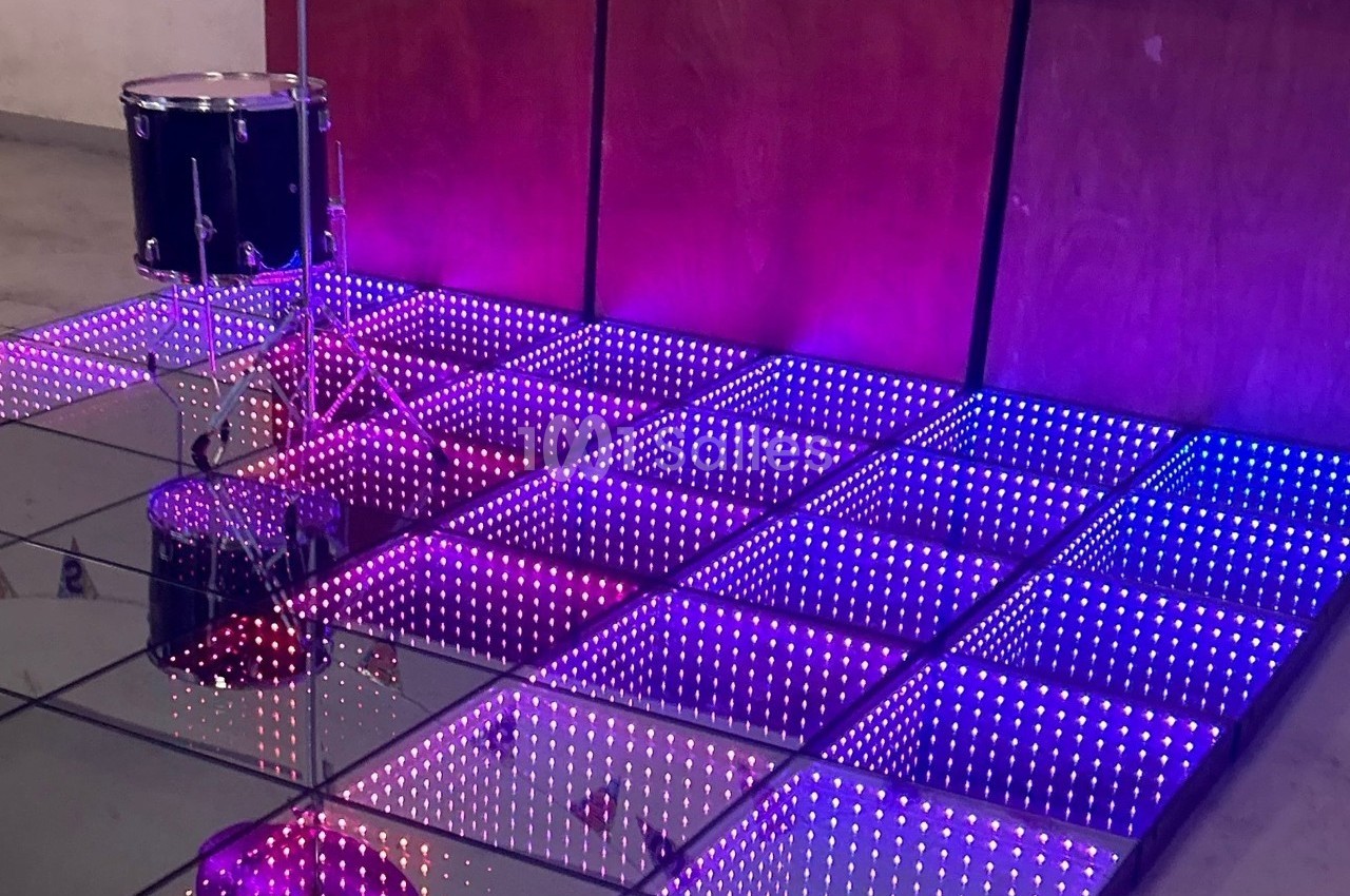 Scène avec un sol lumineux à carreaux LED violets et un tambour installé à côté d'un mur en bois.