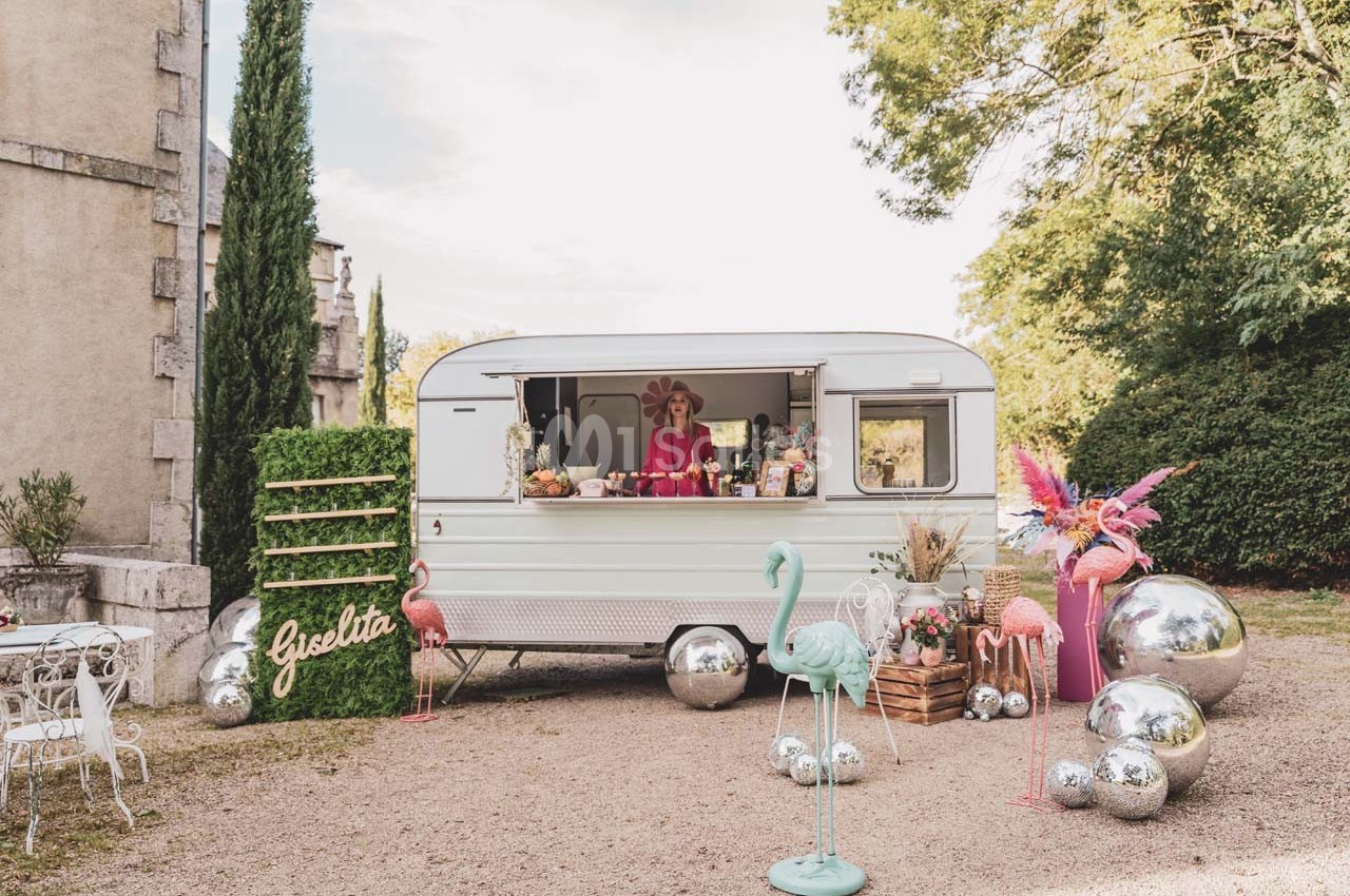 Caravane vintage aménagée en stand, entourée de décorations colorées, flamants roses et boules argentées.