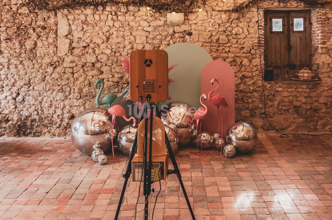Trépied avec appareil photo devant une décoration colorée composée de flamants roses, sphères argentées et panneaux pastel.