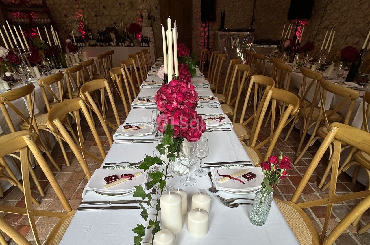 Tables de réception décorées avec des bougies, des fleurs rouges et du lierre, dans une salle en pierre.
