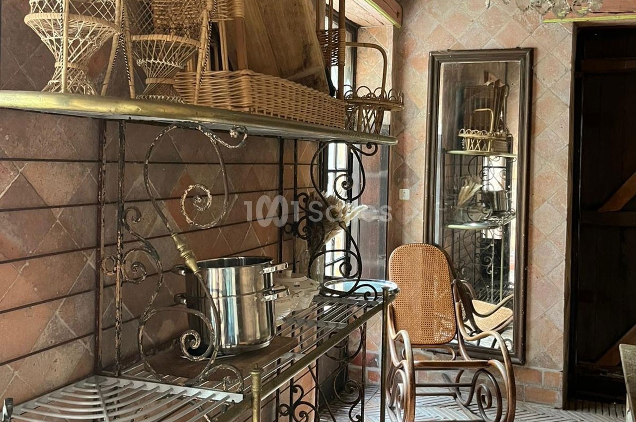 Étagères en métal et osier avec ustensiles de cuisine, chaise en rotin et miroir dans une pièce au mur carrelé.