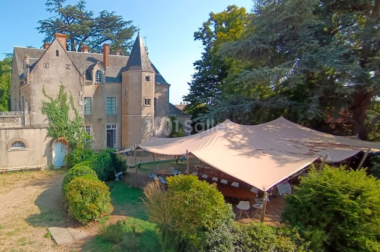 Château ancien entouré de verdure avec une grande tente installée pour un événement en extérieur.