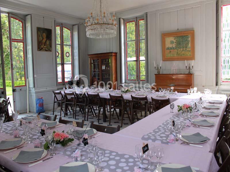 Salle de réception lumineuse avec tables dressées en U, nappes roses et blanches, et décor élégant.