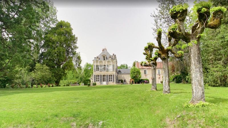 Manoir entouré d'un grand jardin verdoyant avec des arbres taillés et des bâtiments annexes en arrière-plan.