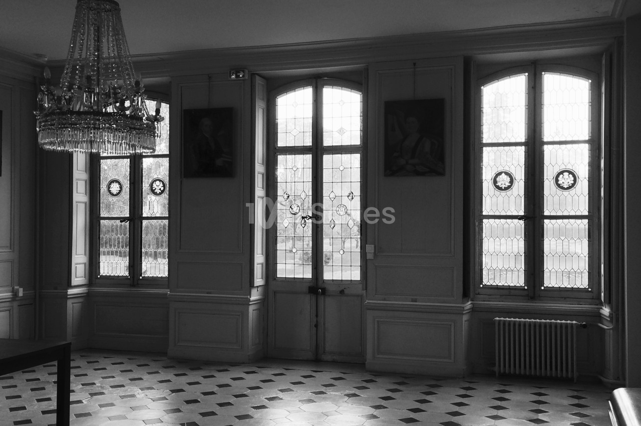 Salle lumineuse avec fenêtres à vitraux, sol en carrelage géométrique et lustre suspendu au plafond.