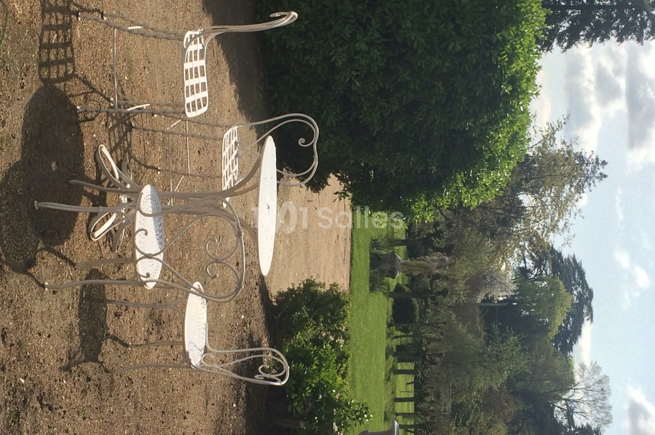 Mobilier de jardin en fer forgé blanc sur une terrasse en gravier, entouré de verdure et d'arbres.