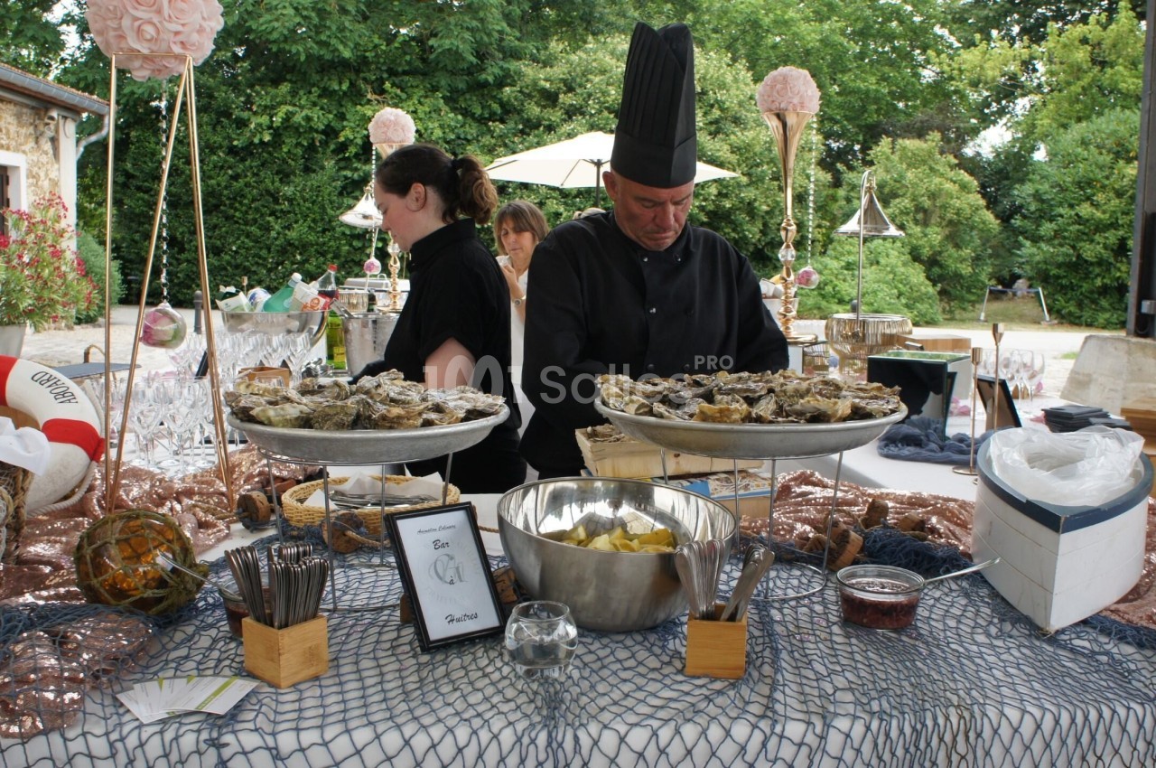 Un chef en tenue noire prépare un buffet d'huîtres en extérieur, entouré de décorations marines.