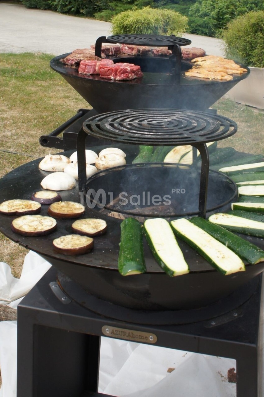 Barbecue circulaire avec légumes grillés, champignons, courgettes, aubergines et viandes en cuisson en plein air.