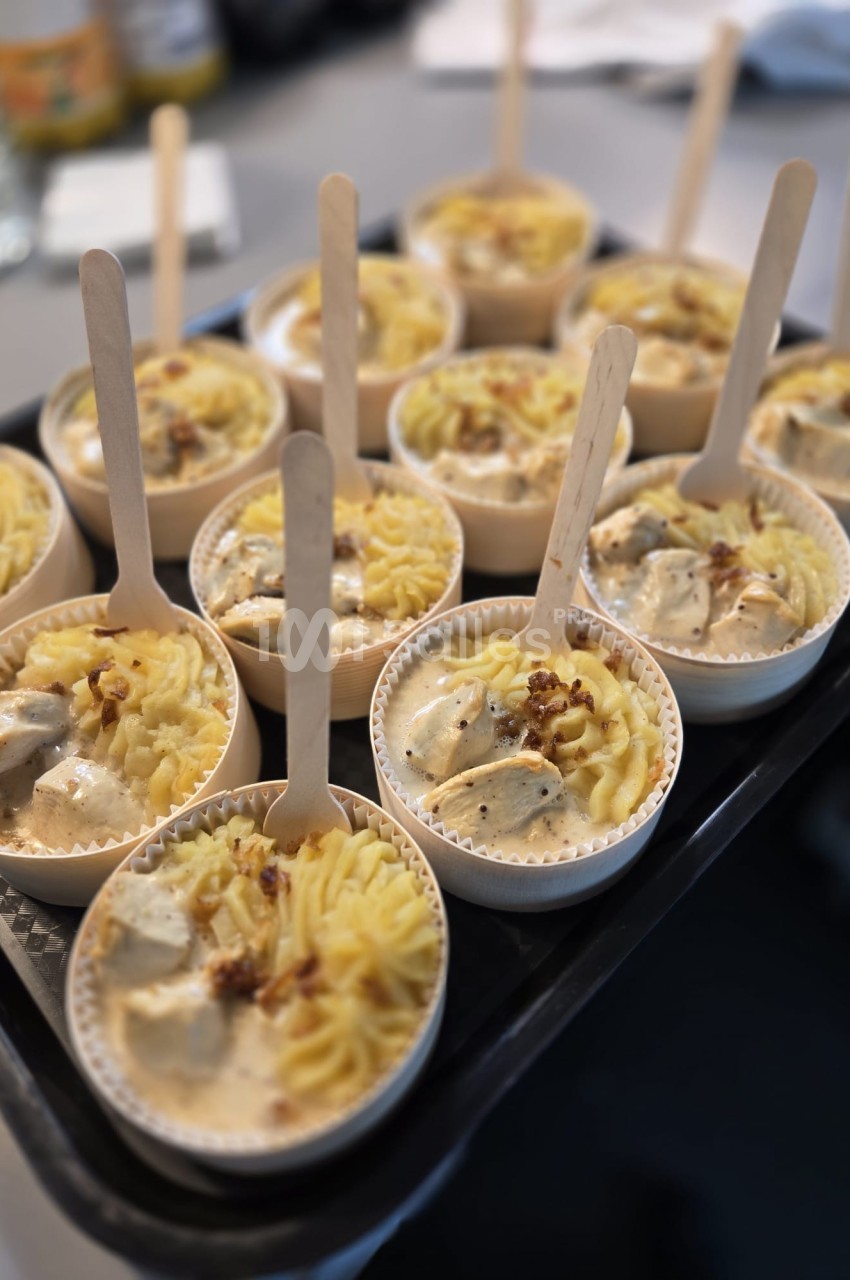 Petits plats individuels contenant purée, morceaux de viande en sauce et cuillères en bois, disposés sur un plateau.