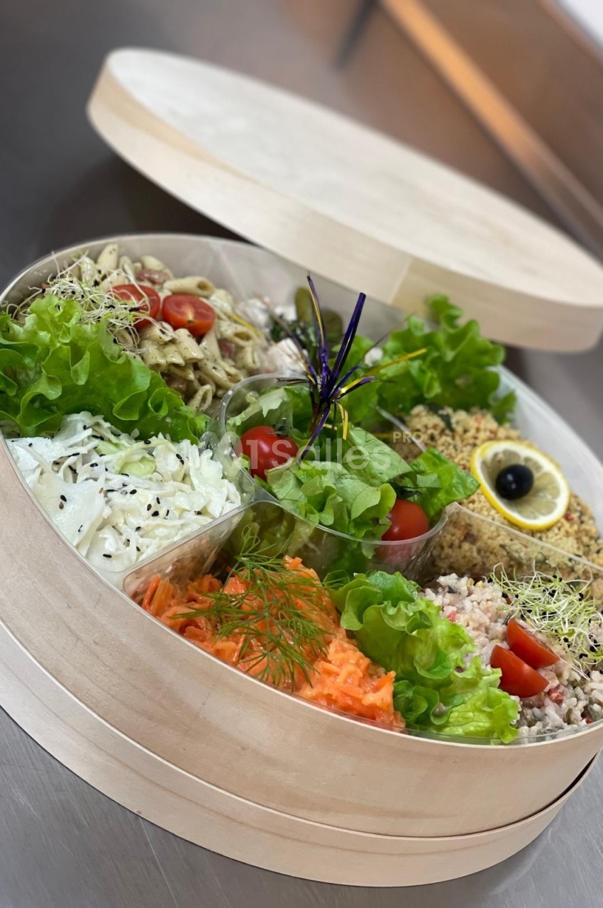 Plateau rond en bois contenant plusieurs compartiments garnis de salades variées, légumes frais et garnitures.