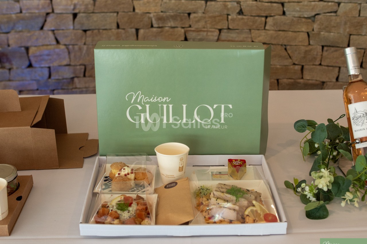 Plateau-repas traiteur avec diverses préparations, présenté sur une table devant une boîte verte et un mur en pierre.
