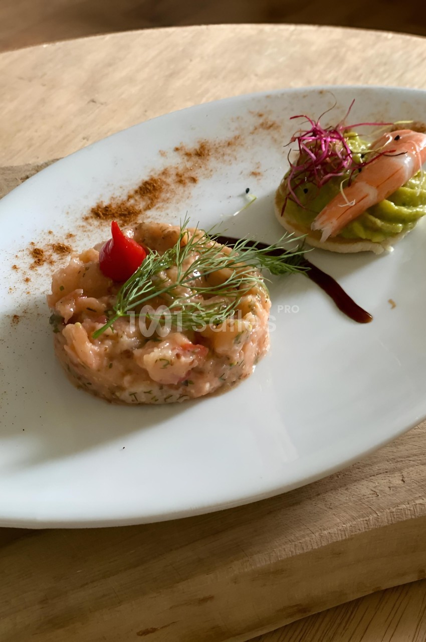 Assiette avec un tartare de saumon garni d'aneth et une bouchée d'avocat, crevette et germes, sur une table en bois.