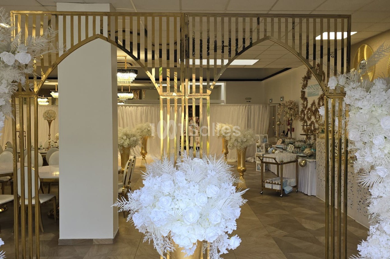 Décoration intérieure élégante avec des arches dorées, des fleurs blanches et un espace aménagé pour un événement.