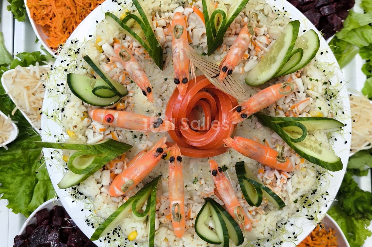 Plateau de salade décorée avec des crevettes, rondelles de concombre et spirales de saumon au centre.