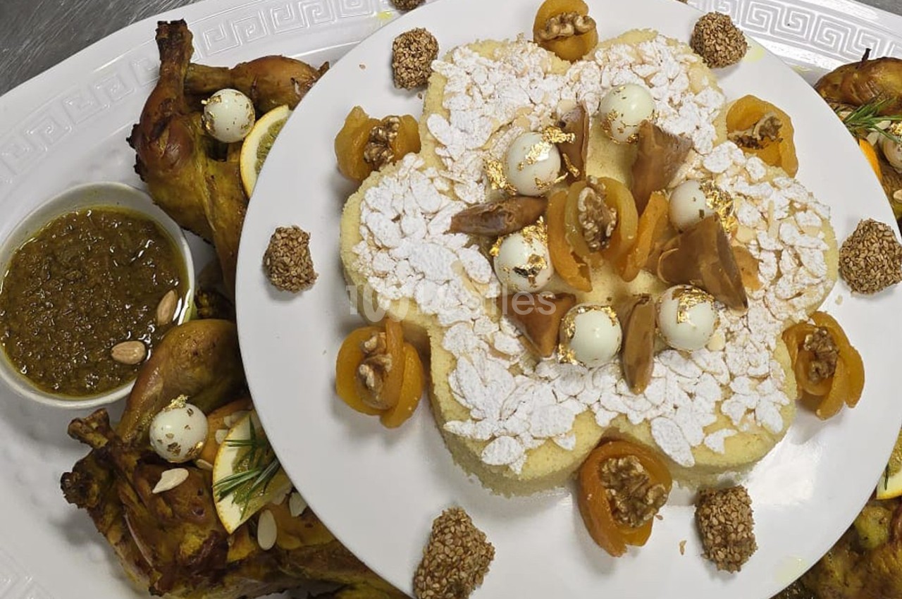 Plat de semoule décoré d'amandes, abricots secs et noix, accompagné de poulet rôti et sauce aux herbes.