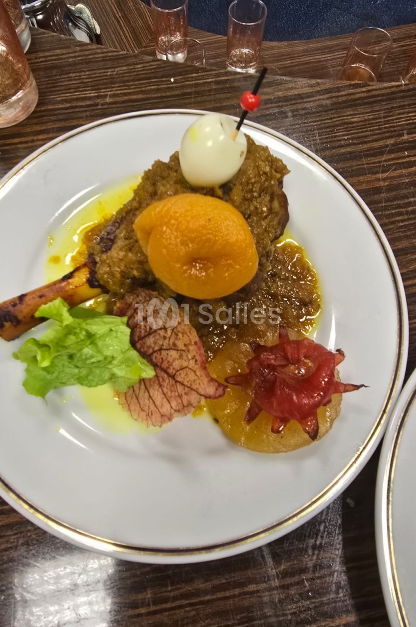 Assiette garnie d'un jarret d'agneau en sauce, accompagnée de légumes, fruits confits et d'une décoration en œuf et cerise.