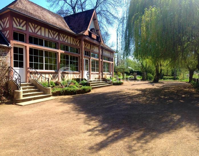 Bâtiment à colombages avec grandes fenêtres, entouré d'arbres et d'un espace extérieur ensoleillé.