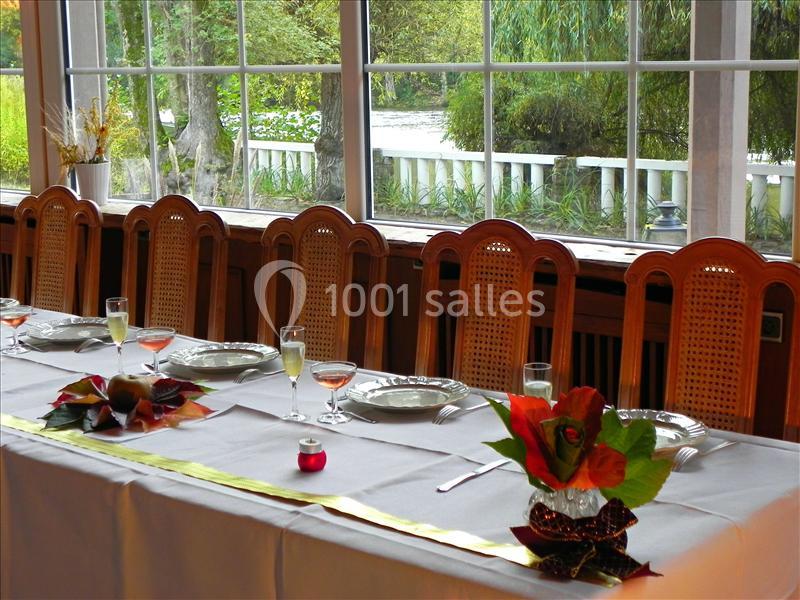 Table dressée avec nappes blanches, vaisselle, verres et décorations florales, près d'une grande baie vitrée donnant sur un…