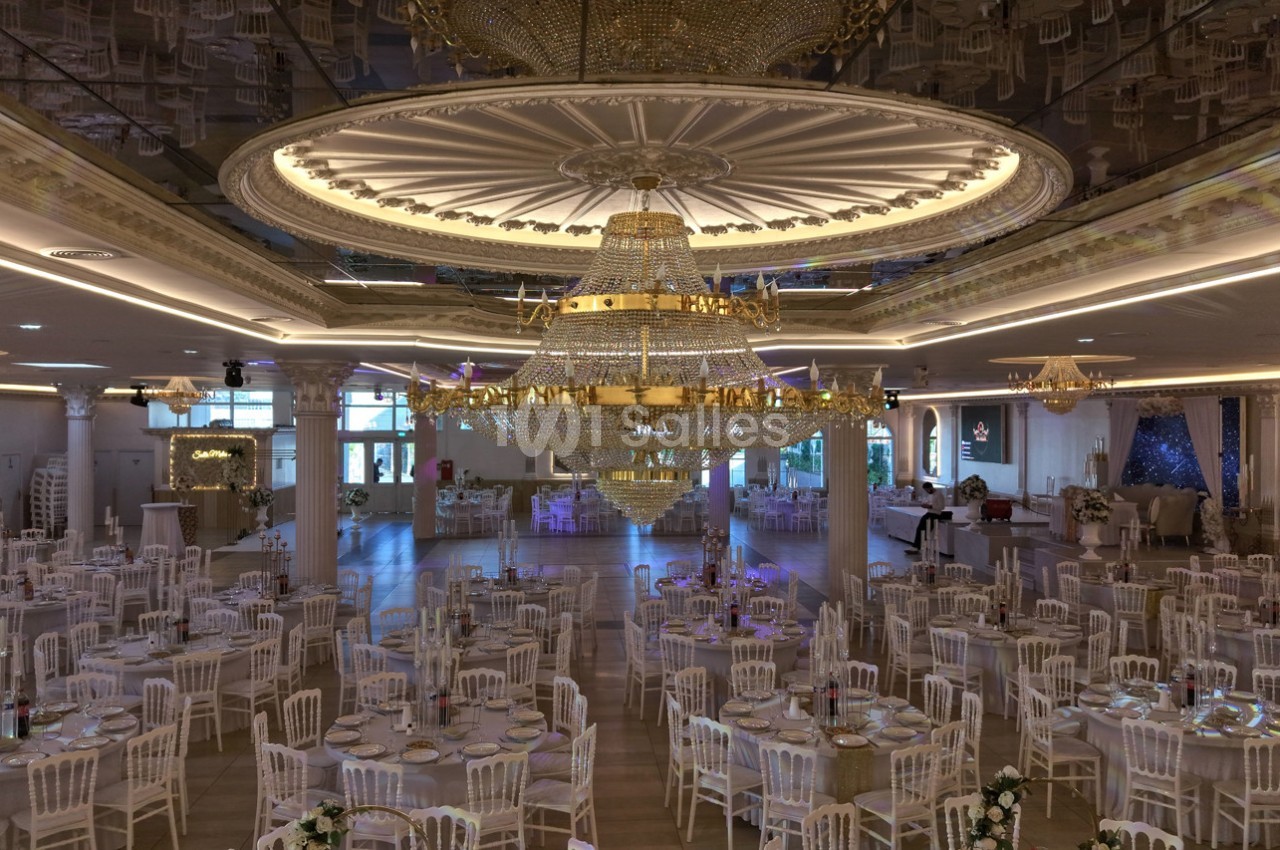 Salle de réception élégante avec de grandes tables dressées et un imposant lustre central en cristal.