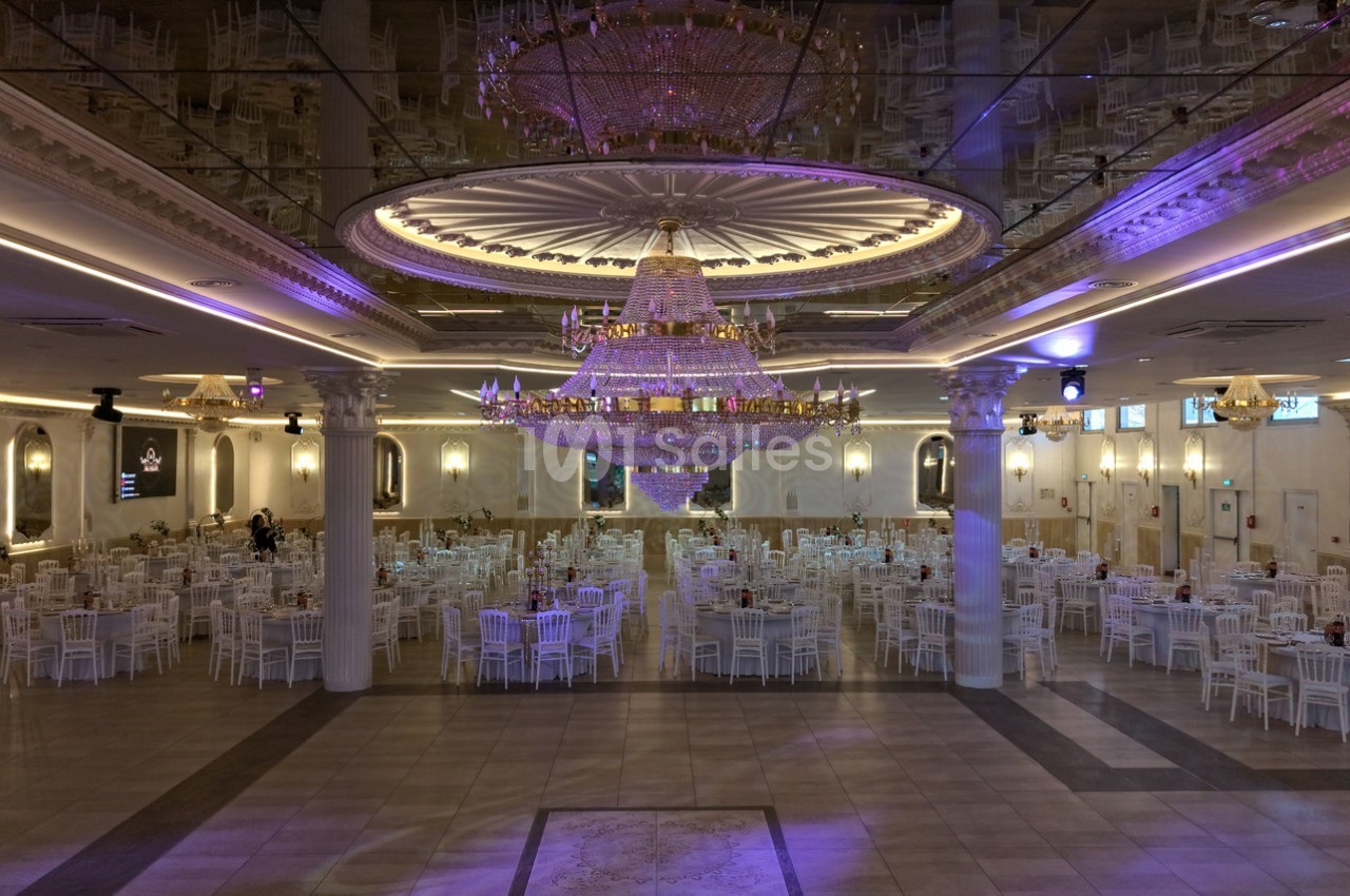 Salle de réception élégante avec un grand lustre central, des tables rondes et des chaises blanches disposées symétriquement.