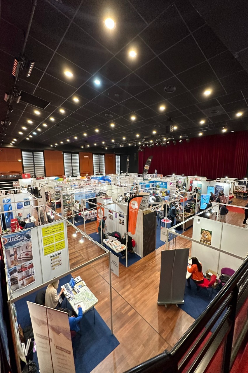 Vue plongeante sur un salon professionnel avec des stands alignés, des visiteurs et une salle éclairée.