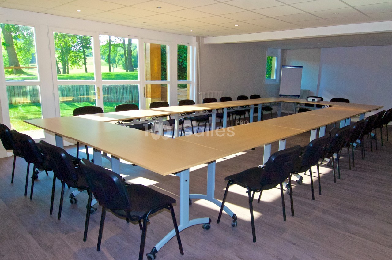 Salle de réunion lumineuse avec une grande table en U, des chaises noires et un tableau de présentation.