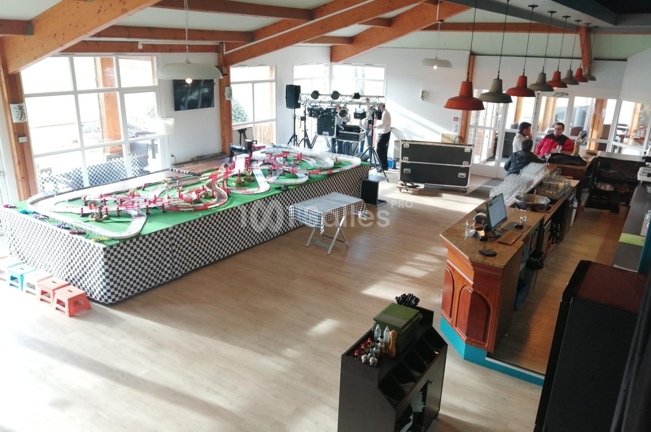 Salle lumineuse avec un circuit de voitures miniatures, un bar en bois et des équipements techniques en arrière-plan.