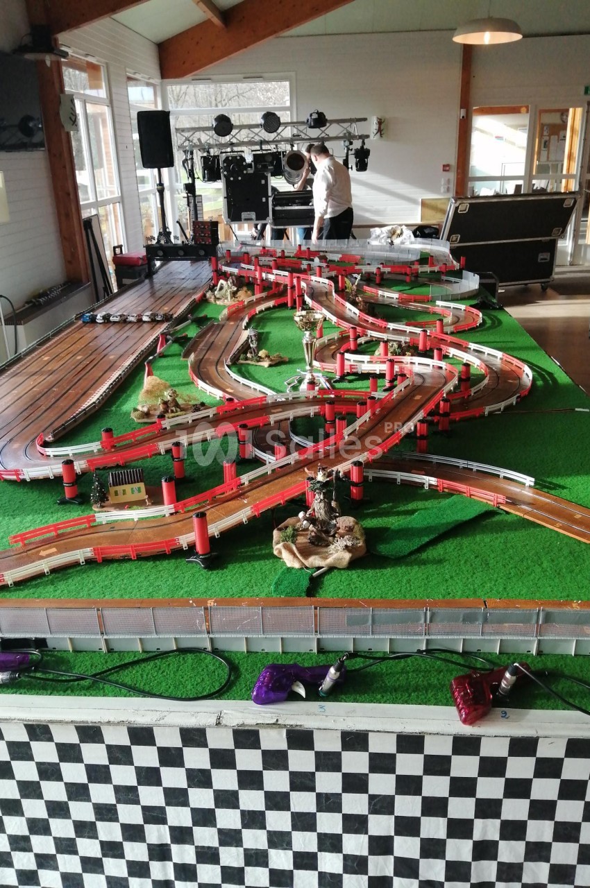 Circuit de course miniature avec des pistes sinueuses, des décors et des structures sur une table dans une salle.