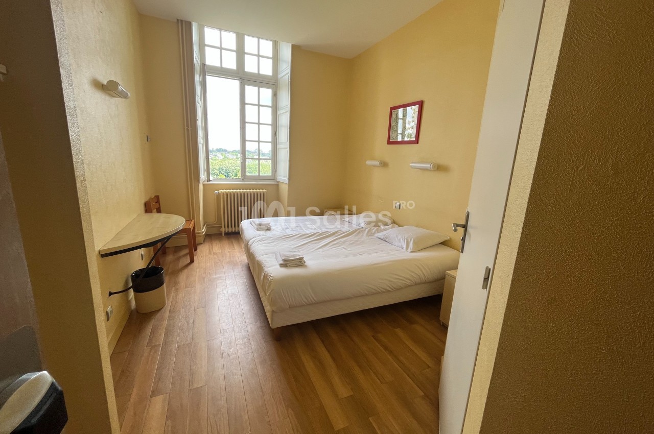 Chambre lumineuse avec deux lits simples, parquet au sol, bureau, chaise et grande fenêtre donnant sur l'extérieur.