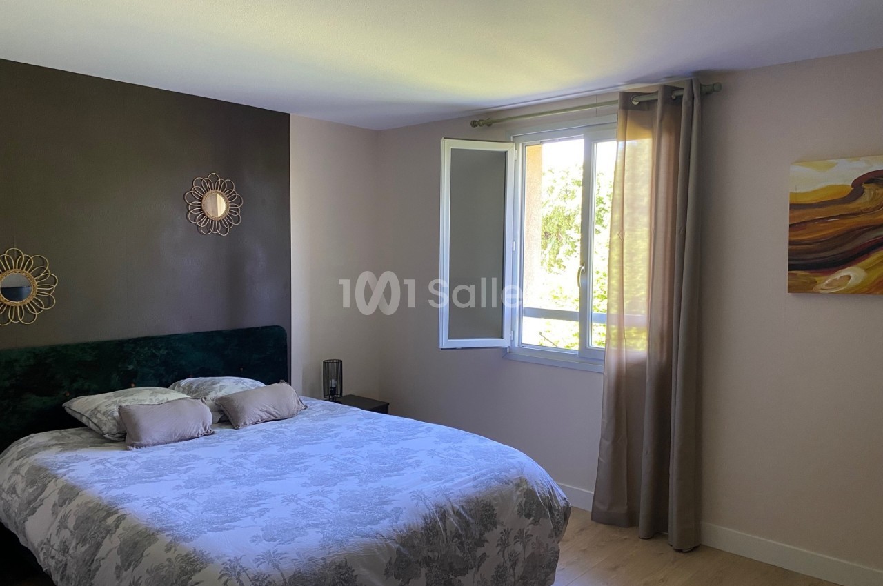 Chambre lumineuse avec lit double, mur accent marron, miroir décoratif, fenêtre ouverte et rideaux beiges.